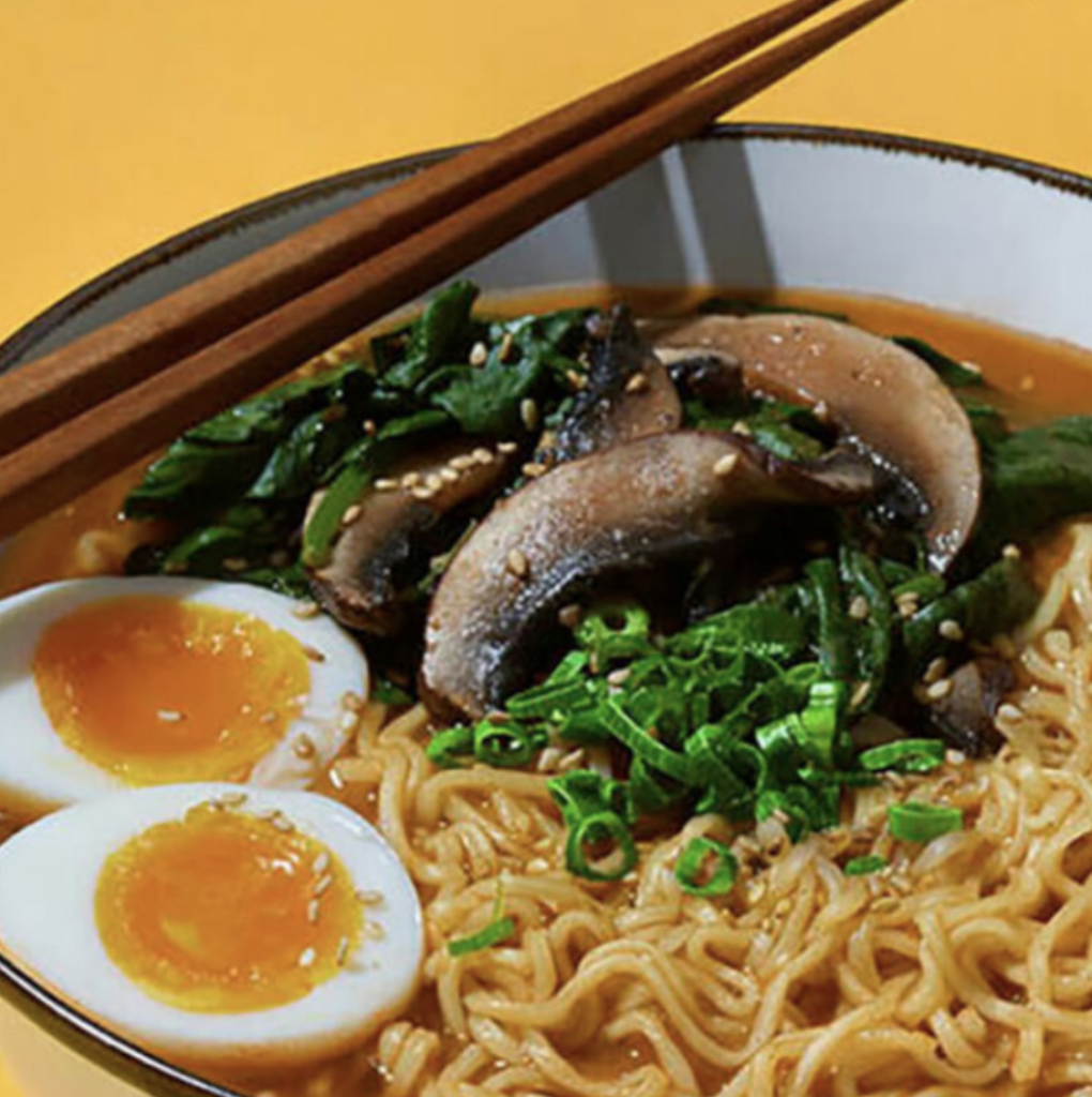 A bowl of ramen noodles, with egg and mushroom, against a yellow background
